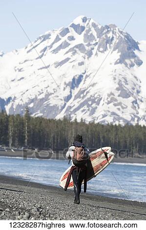 Stock Photograph - Surfer Walking With Surfboard Along The Kenai Peninsula Outer Coast, Southcentral Alaska, USA. Fotosearch