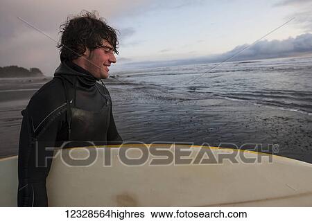Stock Photograph - Surfer with board at sunset, Southeast Alaska; Yakutat, Alaska, United States of America. Fotosearch