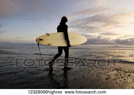 Stock Photograph - Surfer with board at sunset, Southeast Alaska; Yakutat, Alaska, United States of America. Fotosearch