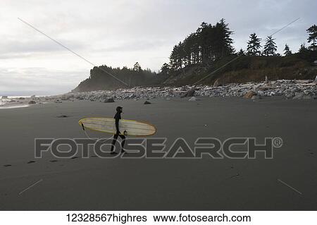 Stock Photograph - Surfer with his board leaving footprints on the beach, Southeast Alaska; Yakutat, Alaska, United States of America. Fotosearch