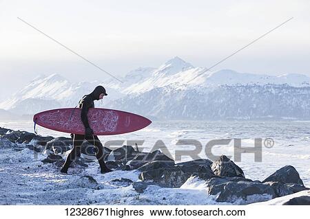 Stock Photograph - Surfer with surfboard entering Kachemak Bay, South-central Alaska; Homer, Alaska, United States of America. Fotosearch