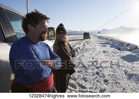 Stock Photograph - Surfers stand along Homer Spit Road in winter looking out to Kachemak Bay, South-central Alaska; Homer, Alaska, United States of America. Fotosearch