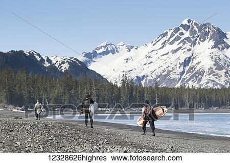 Stock Photograph - Surfers walking on the beach along the Kenai Peninsula Outer Coast, South-central Alaska, USA. Fotosearch