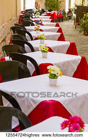 Tables set on an outdoor patio at a restaurant in Italy with a male tourist sitting and using his smart phone; Syracuse, Sicily, Ortigia, Italy View Large Photo Image Stock Photograph - Tables set on an outdoor patio at a restaurant in Italy with a male tourist sitting and using his smart phone; Syracuse, Sicily, Ortigia, Italy. Fotosearch