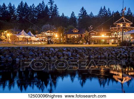 Stock Photograph - The heritage site tourist attraction Union Steamship Building in Snug Cove, Bowen Island is lit up at night welcoming tourists to the restaurant, shops and marina a quick ferry ride from Vancouver, BC; Bowen Island, British Columbia, Canada. Fotosearch