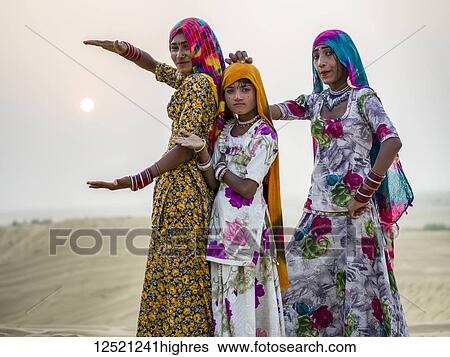 Stock Photograph - Three Indian women in a silly pose in the Sam sand dunes with a glowing sun in the distance, Thar Desert; Hanoi, Rajasthan, India. Fotosearch