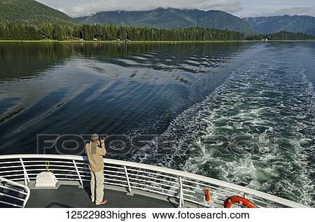 Stock Photograph - Tourist photographing Wrangell Narrows looking North toward Petersburg from stern of Alaska State Ferry, Southeast Alaska; Alaska, United States of America. Fotosearch