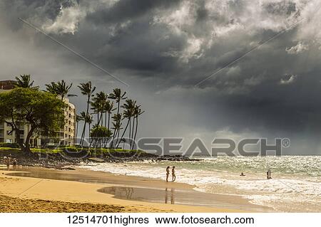 Stock Photograph - Tourists on a beach on the island of Maui with dark clouds and rainfall over the ocean in the distance; Makawao, Maui, Hawaii, United States of America. Fotosearch