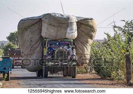 Stock Photograph - Truck carrying a huge load of wheat in Northern India with three men riding on the front of the truck; Rajasthan, India. Fotosearch