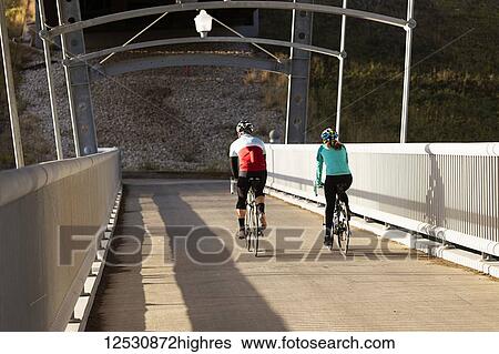 Two Cyclists Riding Across A Concrete Bridge On A Fall Evening; Edmonton, Alberta, Canada View Large Photo Image Stock Photograph - Two Cyclists Riding Across A Concrete Bridge On A Fall Evening; Edmonton, Alberta, Canada. Fotosearch