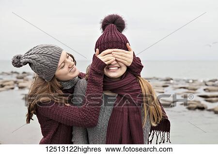 Stock Photograph - Two friends playing on the beach wearing knit hats and scarves, Woodbine Beach; Toronto, Ontario, Canada. Fotosearch