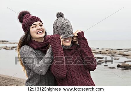 Stock Photograph - Two friends playing on the beach wearing knit hats and scarves, Woodbine Beach; Toronto, Ontario, Canada. Fotosearch