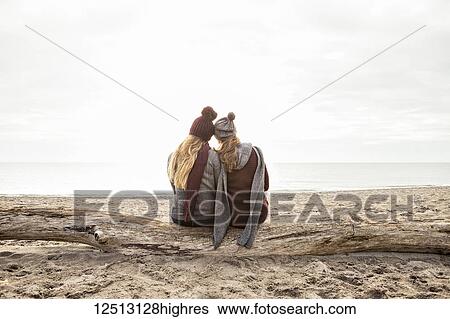 Stock Photograph - Two friends sitting on a log on Woodbine beach looking out to Lake Ontario; Toronto, Ontario, Canada. Fotosearch