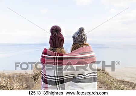 Stock Photograph - Two friends wrapped in a blanket standing on bluffs looking out over Lake Ontario; Scarborough, Ontario, Canada. Fotosearch