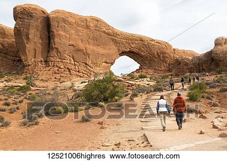 Stock Photograph - Two hikers approaching Window Arch, Arches National Park, Utah, United States of America. Fotosearch