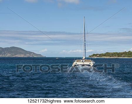 Stock Photograph - Two men sailing a catamaran sailing near island of Nevis in the Caribbean; Nevis, West Indies. Fotosearch