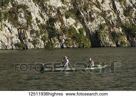 Two men sitting in a wooden boat with motor and fishing in the Danube River with a rock cliff in the background; Golubinje, Majdanpek, Serbia View Large Photo Image Stock Photograph - Two men sitting in a wooden boat with motor and fishing in the Danube River with a rock cliff in the background; Golubinje, Majdanpek, Serbia. Fotosearch
