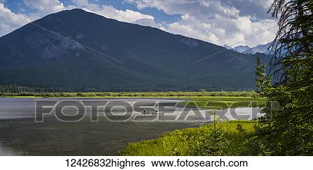 Stock Photograph - Two people sit in a canoe in the tranquil water of Vermillion Lakes in the Canadian Rocky Mountains; Field, Alberta, Canada. Fotosearch