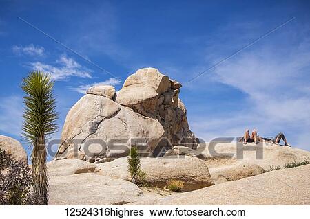 Stock Photograph - Two people sunbathing on a rock in Joshua Tree National Park; California, United States of America. Fotosearch