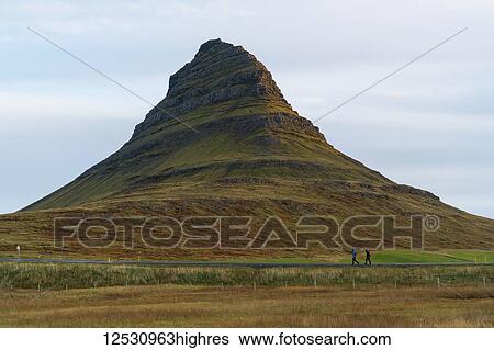 Stock Photograph - Two people walking along the road in front of Kirkjufell, Snaefellsness Peninsula; Iceland. Fotosearch