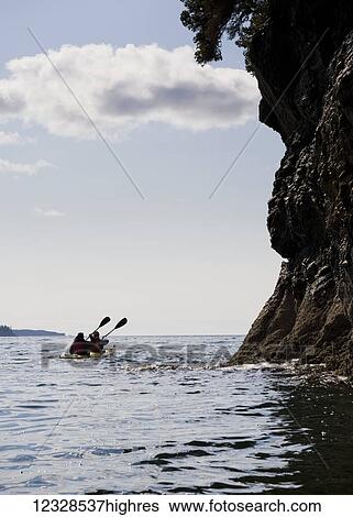 Stock Photograph - Two sea kayakers in a double sea kayak, Kachemak Bay, Southcentral Alaska; Alaska, United States of America. Fotosearch