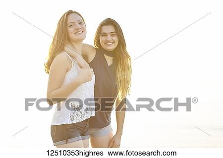Stock Photograph - Two teenage girls posing for the camera as they stand in an embrace and bathed in warm sunlight, Woodbine Beach; Toronto, Ontario, Canada. Fotosearch
