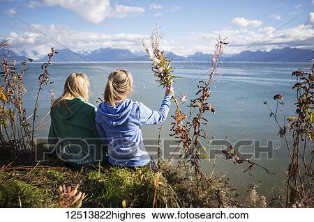 Stock Photograph - Two women sit on bluff overlooking Kachemak Bay on an autumn day, South-central Alaska; Homer, Alaska, United States of America. Fotosearch