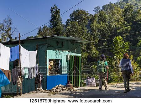 Stock Photograph - Two women walking on a road past a colourful house and a clothesline; West Bengal, India. Fotosearch