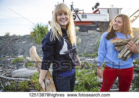 Stock Photograph - Two young women gathering firewood along coastal Homer, South-central Alaska; Homer, Alaska, United States of America. Fotosearch