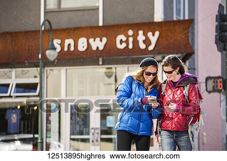 Two young women look at a smart phone while outside a popular restaurant in downtown Anchorage, South-central Alaska; Anchorage, Alaska, United States of America View Large Photo Image Stock Photograph - Two young women look at a smart phone while outside a popular restaurant in downtown Anchorage, South-central Alaska; Anchorage, Alaska, United States of America. Fotosearch