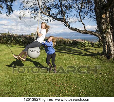 Two young women playing on a buoy rope swing, South-central Alaska; Homer, Alaska, United States of America View Large Photo Image Stock Photograph - Two young women playing on a buoy rope swing, South-central Alaska; Homer, Alaska, United States of America. Fotosearch