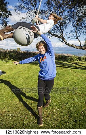 Stock Photograph - Two young women playing on a buoy rope swing, South-central Alaska; Homer, Alaska, United States of America. Fotosearch