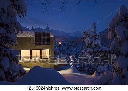 Warm light spills from a cabin in a snow-covered landscape, solar panels on the roof of the cabin, cool light at dusk casts soft light on distant snow-covered Kenai Mountains, South-central Alaska in winter; Moose Pass, Alaska, United States of America View Large Photo Image Stock Photograph - Warm light spills from a cabin in a snow-covered landscape, solar panels on the roof of the cabin, cool light at dusk casts soft light on distant snow-covered Kenai Mountains, South-central Alaska in winter; Moose Pass, Alaska, United States of America. Fotosearch
