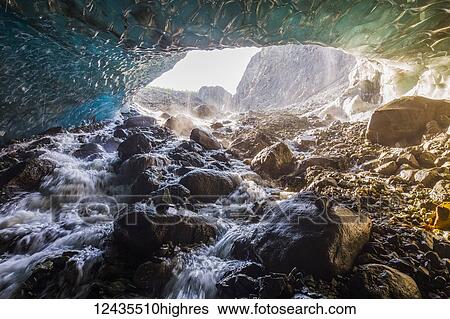 Stock Photograph - Water cascades over rocks inside a cave beneath the ice of Root Glacier in Wrangell-St. Elias National Park; Alaska, United States of America. Fotosearch