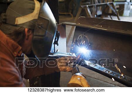 Stock Photograph - Welder And Metal Work Artist Doug Schwiesow Working On A Custom Sign Designed With A Local Artist For The Kenai Peninsula College Kachemak Bay Campus.. Fotosearch