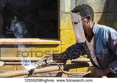 Stock Photograph - Welder at the Medeber Market, where artisans recycle old tyres and tins to make new artifacts; Asmara, Central Region, Eritrea. Fotosearch