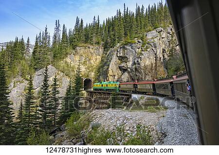 Stock Photograph - White Pass Railroad enters tunnels as it transports tourists on ride out of Skagway Alaska into Canada and returns; Skagway, Alaska, United States of America. Fotosearch