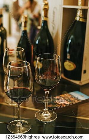 Stock Photograph - Wine bottles and glasses of red wine with a pamphlet on the table; Italy. Fotosearch