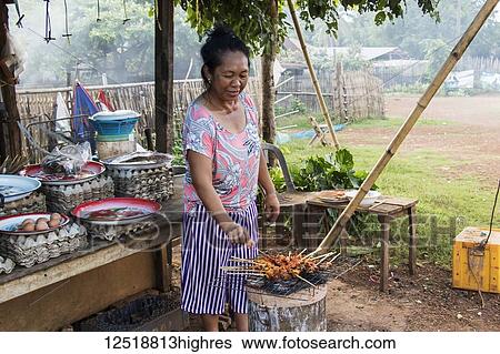 Stock Photograph - Woman barbecuing satay, Pha Suam, Bolaven Plateau; Champasak, Laos. Fotosearch