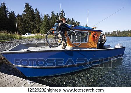 Stock Photograph - Woman loads her bike on to a water taxi, Kenai Peninsula, South-central Alaska; Alaska, United States of America. Fotosearch