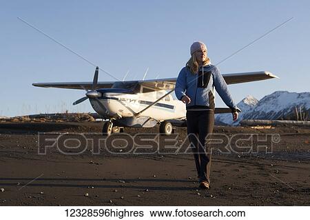 Stock Photograph - Woman on a beach with a bush plane in the background, Kachemak Bay State Park, South-central Alaska; Alaska, United States of America. Fotosearch