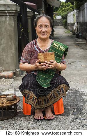 Stock Photograph - Woman waiting to give Buddhist monks alms on Khounsua Road at dawn; Luang Prabang, Luang Prabang, Laos. Fotosearch