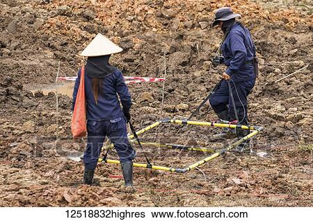Stock Photograph - Women using a metal detector while clearing landmines in a field near Phonsavan; Xiangkhouang, Laos. Fotosearch