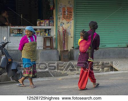 Stock Photograph - Women walk down the street, one with a small child in a sling, 0rthern India; Narendranager, Uttarakhand, India. Fotosearch