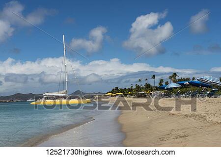 Stock Photograph - Yellow catamaran and striped umbrellas along the beach of a Caribbean Island; Nevis, West Indies. Fotosearch