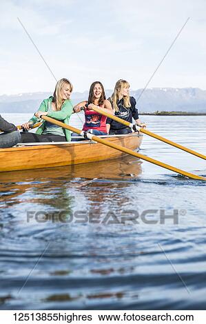 Stock Photograph - Young adults rowing in a canoe, South-central Alaska; Homer, Alaska, United States of America. Fotosearch