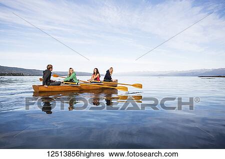 Stock Photograph - Young adults rowing in a canoe, South-central Alaska; Homer, Alaska, United States of America. Fotosearch