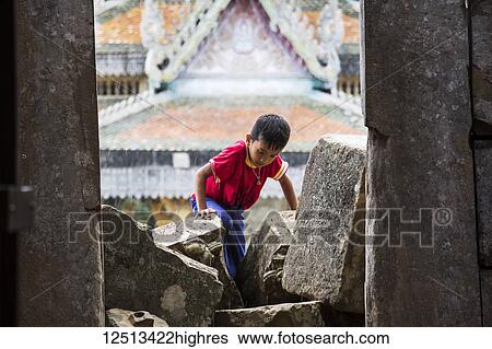 Stock Photograph - Young boy climbing in the ancient Angkorian temple at Wat Ek Phnom; Battambang, Cambodia. Fotosearch