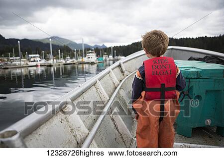 Stock Photograph - Young boy stands in his family's set-net skiff with a life vest saying 'kids don't float', South-central Alaska; Seldovia, Alaska, United States of America. Fotosearch