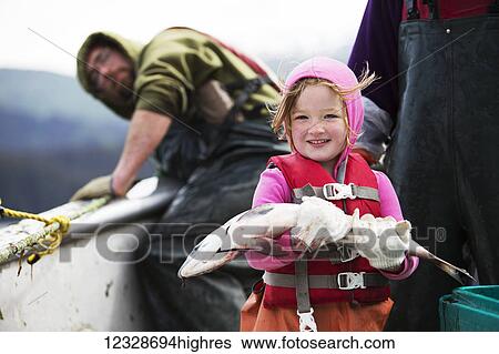 Stock Photograph - Young girl holding a fresh caught salmon while in her family's set-net skiff with her mother, Seldovia, South-central Alaska; Alaska, United States of America. Fotosearch